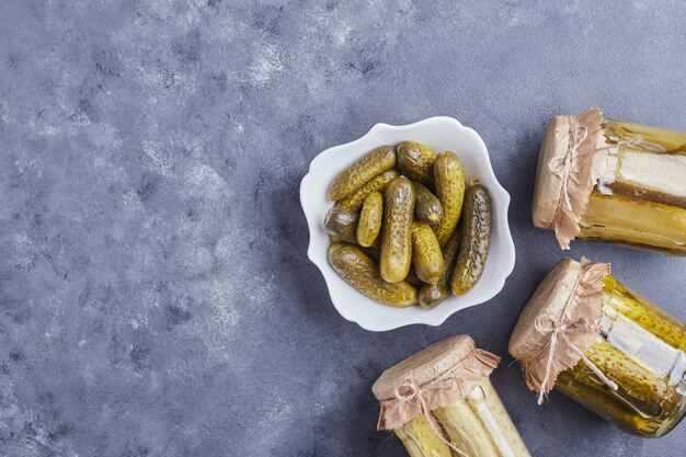 Pickled cucumbers in bowl and glass jars on blue background.