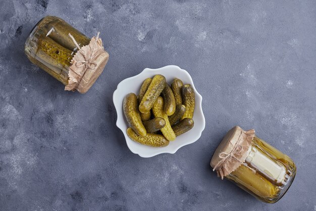 Pickled cucumbers in bowl and glass jars on blue background.