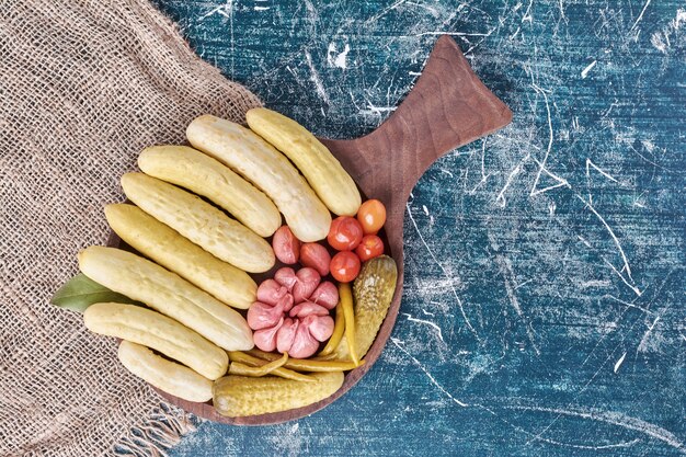 Free photo pickled cucumbers, garlic, peppers and tomatoes on wooden plate.