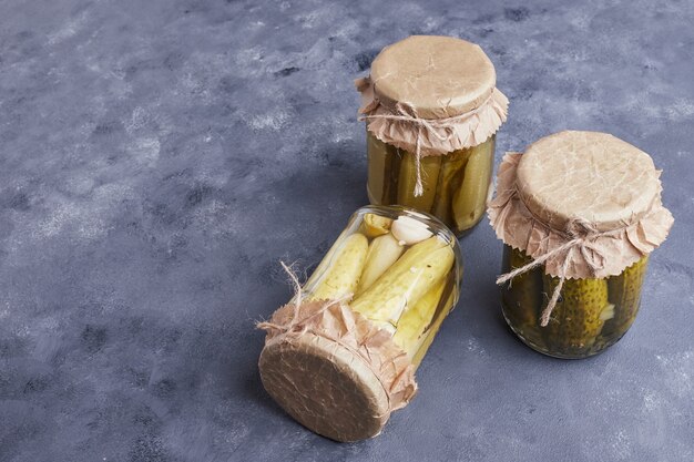 Pickled cucumbers in glass jars on blue background.