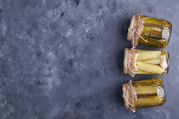 Pickled cucumbers in glass jars on blue background.