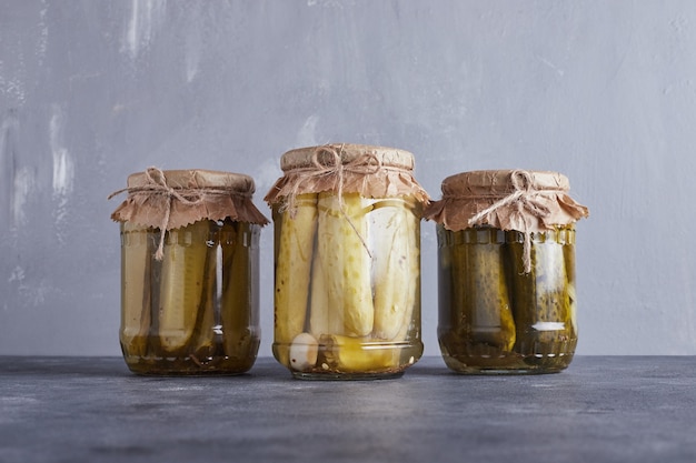 Pickled cucumbers in glass jars on blue background.