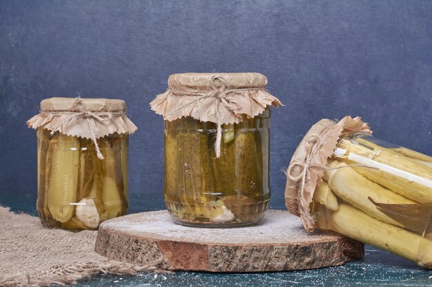 Pickled cucumbers in glass jars on blue. 