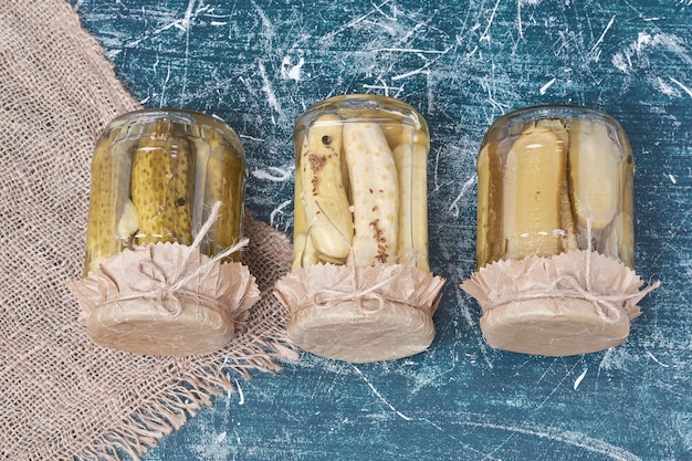 Free photo pickled cucumbers in glass jars on blue.