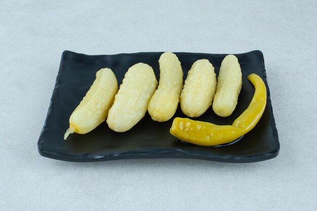 Pickled cucumbers and pepper on black plate.