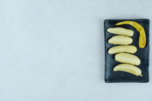 Pickled cucumbers and pepper on black plate.