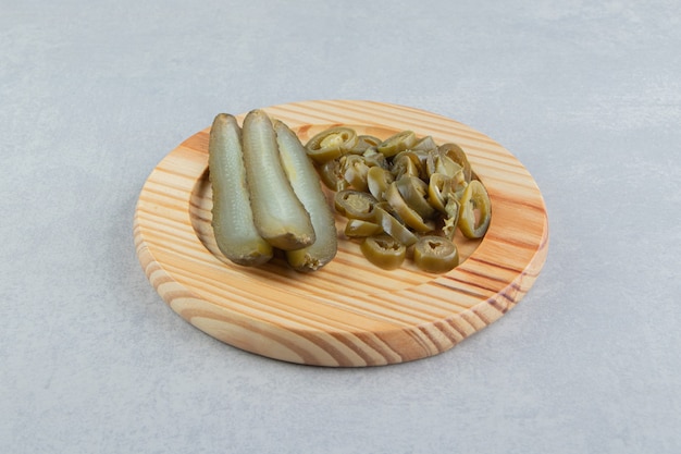 Free photo pickled cucumbers and peppers on wooden plate.