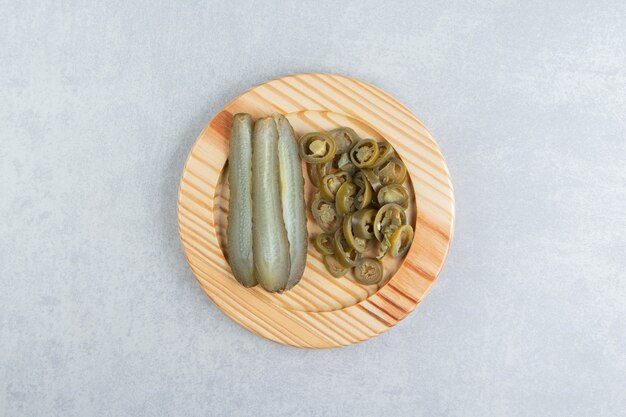 Pickled cucumbers and peppers on wooden plate.  