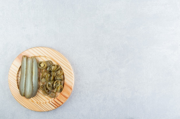 Pickled cucumbers and peppers on wooden plate. 