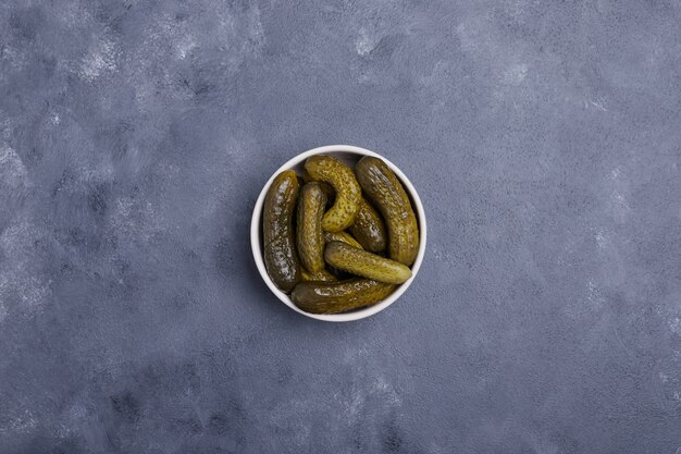 Pickled cucumbers in white bowl on blue background.