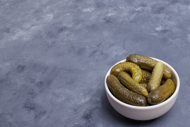 Pickled cucumbers in white bowl on blue background.