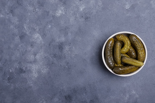 Pickled cucumbers in white bowl on blue background.