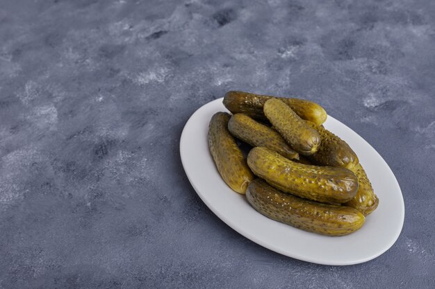 Pickled cucumbers on white plate on blue background.