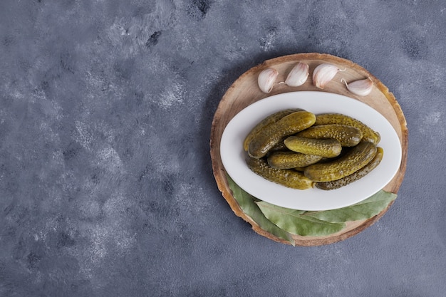 Pickled cucumbers on white plate with garlic on blue background.