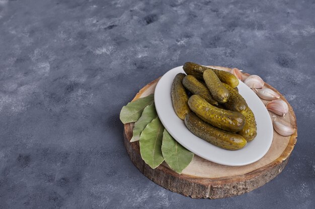 Pickled cucumbers on white plate with garlic on blue background.