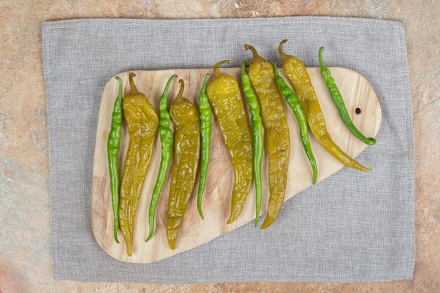 Pickled and fresh green peppers on wooden board