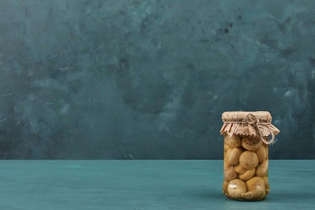 Pickled mushrooms in a glass jar on blue table.