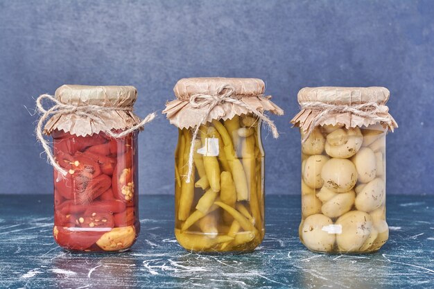 Pickled peppers and mushrooms in a glass jar on blue. 