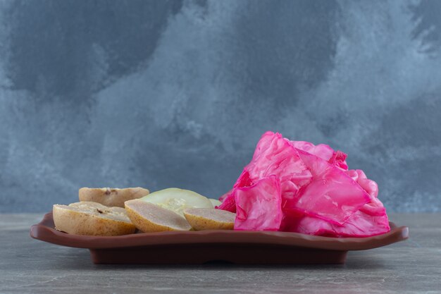 Pickled pink cabbage with apple slices on brown plate.