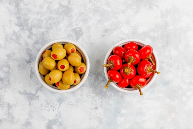 Pickled small round red hot cherry chili peppers on grey concrete 