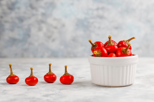 Pickled small round red hot cherry chili peppers on grey concrete 