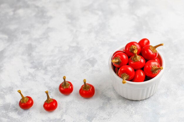 Pickled small round red hot cherry chili peppers on grey concrete 