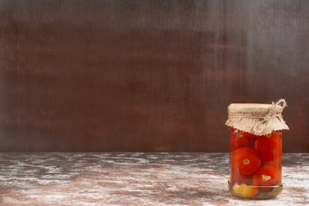 Pickled tomatoes in glass jar on marble table.