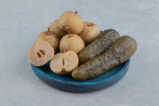 Pickles cucumber and apples on wooden plate on the marble surface