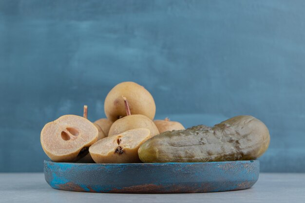 Соленья огурцы и яблоки на деревянной тарелке