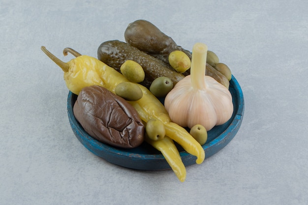 Pickles hot peppers, olive, cucumber and eggplant on the wooden plate on the marble surface