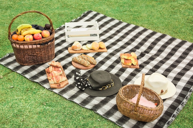 新鮮な果物のピクニックバスケット;焼かれたパンと緑の草の上の毛布に帽子