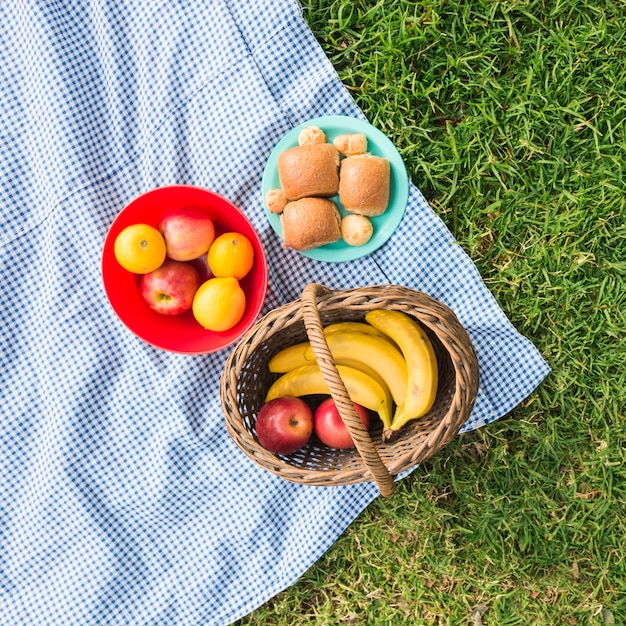 Foto gratuita cestino di picnic con frutta e pane sulla coperta di controllo sopra l'erba verde