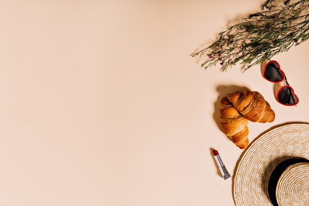 Picnic set of croissants, hat, glasses and cute little flowers lie on beige wall