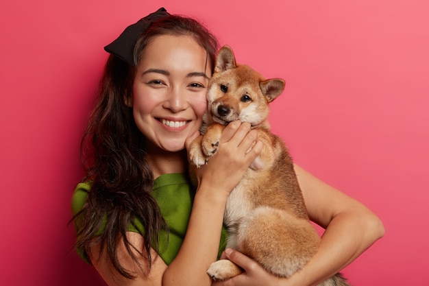 Picture of adorable young girl with toothy smile, embraces and makes photo with beautiful obedient shiba inu dog, enjoys playing with four legged friend.