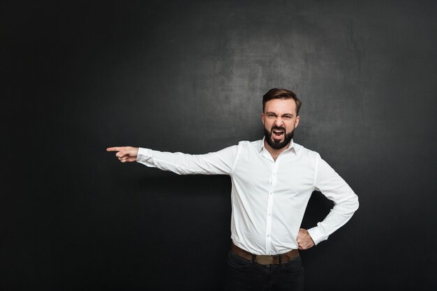 Picture of angry male employer screaming in outrage and pointing finger at door to get out over dark gray