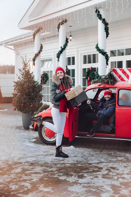 Picture of attractive caucasian woman in warm clothes carries boxes with Christmas gifts in a car to her boyfriend
