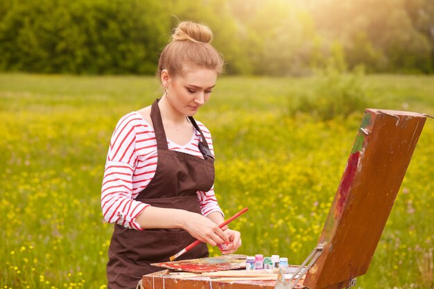 Picture of attractive concentrated young Caucasian female standing with palette of colours