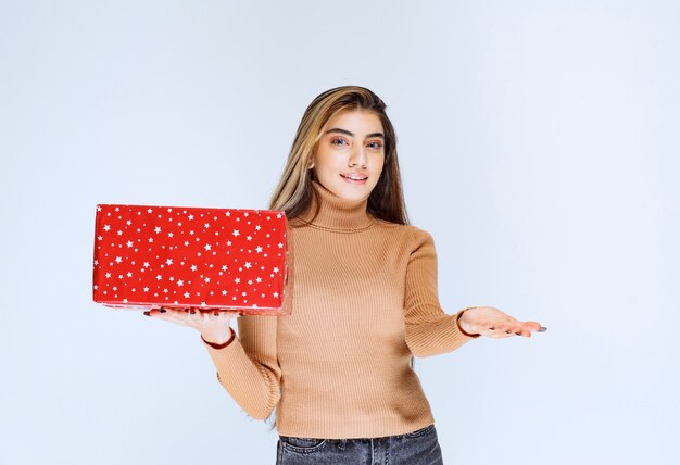 Изображение модели привлекательной женщины, держащей красный подарок.