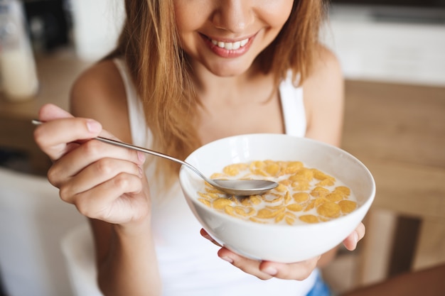 キッチンで牛乳とコーンフレークを食べる魅力的な若い女の子の写真