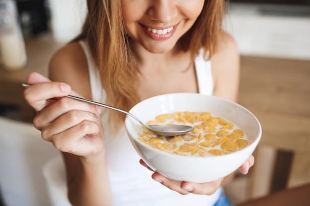 Picture of attractive young girl eating cornflakes with milk at kitchen