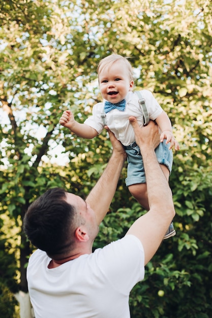 Picture of beautiful caucasian dad holds his little pretty son on the hands and they rejoices together outside in summer