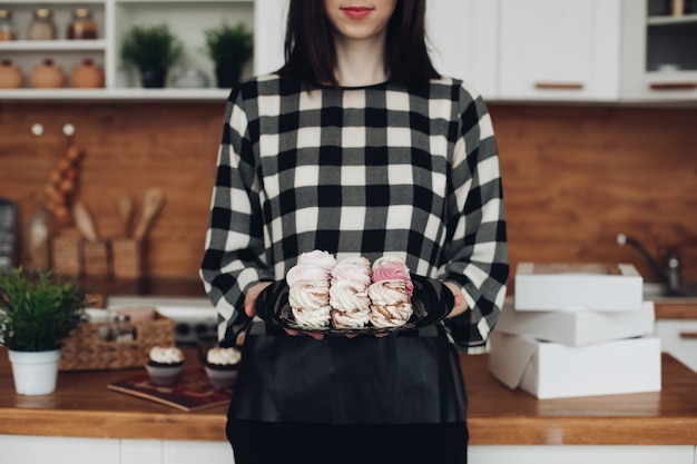 Picture of beautiful caucasian female with short dark hair in black and white sweater holds a box with marshmallows