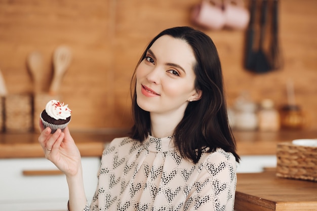 Free photo picture of beautiful caucasian female with short dark hair in a cozy sweater holds a marshmallow and smiles