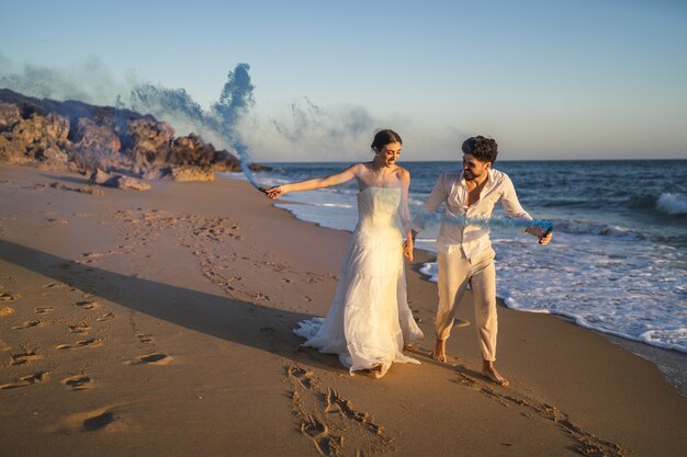 Picture of a beautiful couple posing with a blue smoke bomb in the beach