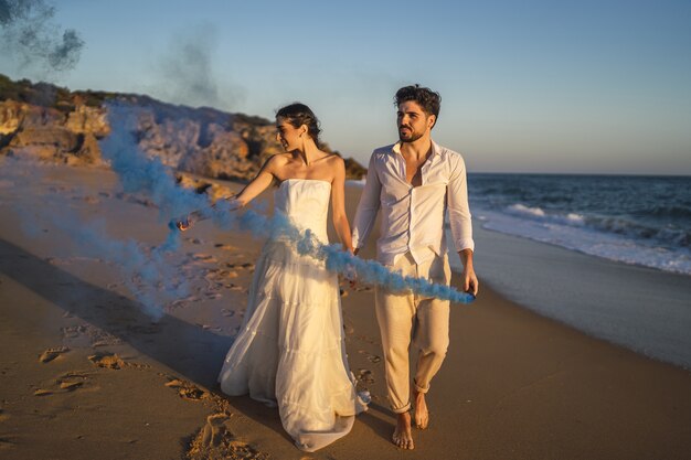 ビーチで青い発煙弾でポーズをとる美しいカップルの写真