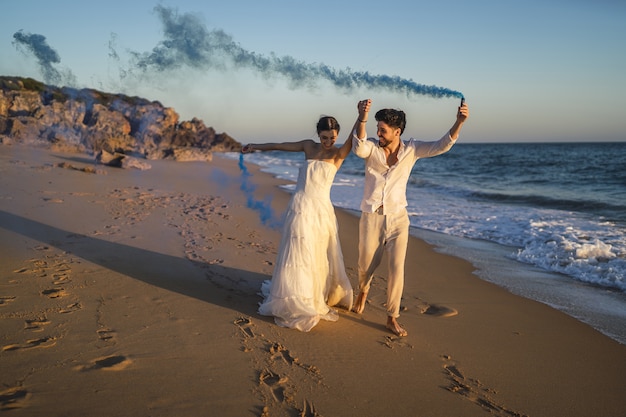 ビーチで青い発煙弾でポーズをとる美しいカップルの写真