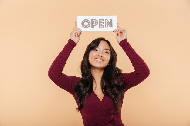 Free photo picture of beautiful woman in maroon dress holding sign with word open over head being friendly on peach background