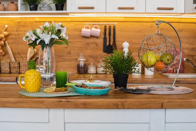 Picture of the big bright kitchen with white and brown cupboards with yellow pineapple tea kettle, white pepper mill and metal hanging with fruits and cookies