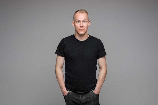 Free photo picture of caucasian man keeps his hands in the pockets of his black jeans isolated on grey wall