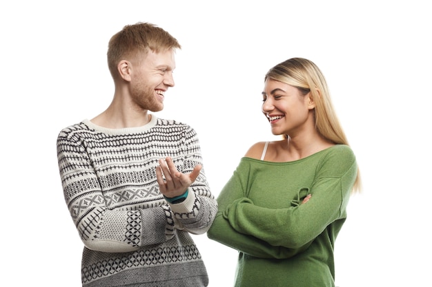 Picture of charismatic guy with stubble smiling happily while telling funny story to attractive young female with fair hair who laughing at his jokes. Cute couple talking